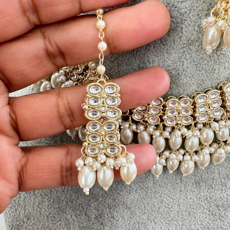 May include: A gold necklace with a row of clear stones and a fringe of white pearls. The necklace is paired with matching earrings with a similar design.