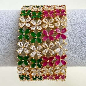 Puede incluir: Un brazalete de oro con un diseño floral. El brazalete está adornado con piedras preciosas transparentes, verdes y rosas.