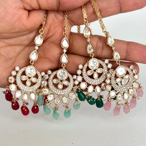 Może przedstawiać: Cztery złote nakrycia głowy o skomplikowanych wzorach. Każdy element ma okrągły element centralny z przezroczystymi kamieniami i kwiatowym wzorem, otoczony mniejszymi kamieniami. Kamienie w kształcie łezki i okrągłe zwisają poniżej w kolorze czerwonym, zielonym i różowym.