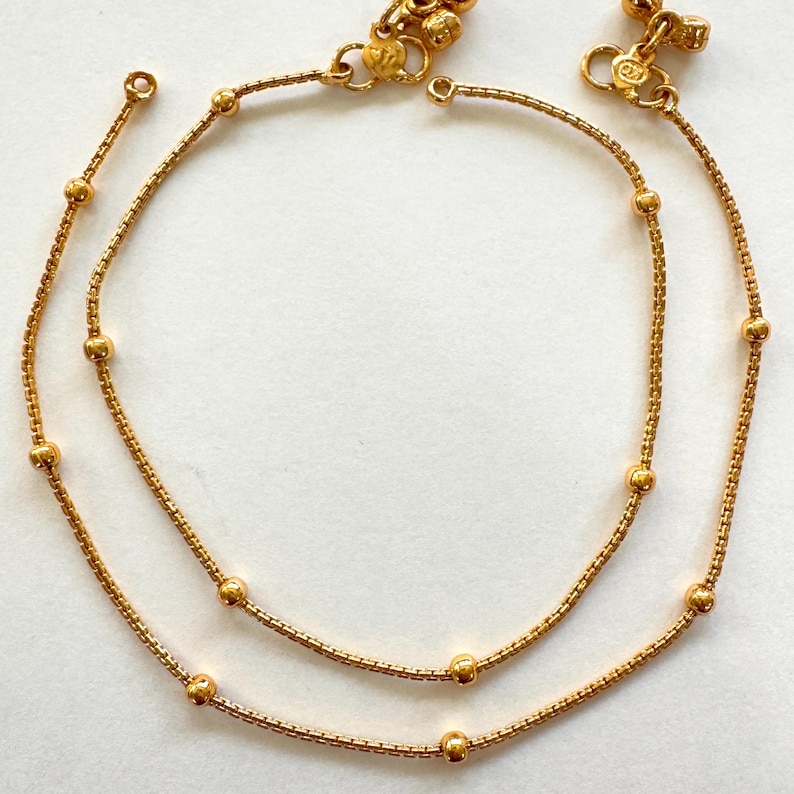K&ouml;nnte beinhalten: Zwei goldene Fu&szlig;kettchen mit kleinen runden Perlen. Die Fu&szlig;kettchen bestehen aus einer zarten Kette und haben ein schlichtes Design.