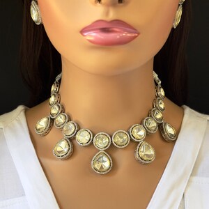 May include: A silver and white crystal necklace with a teardrop design. The necklace features round and teardrop-shaped crystals.