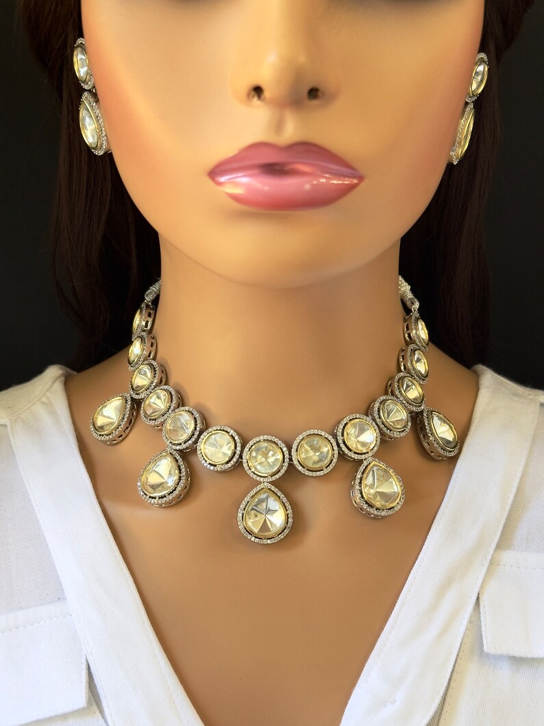 May include: A silver and white crystal necklace with a teardrop design. The necklace features round and teardrop-shaped crystals.
