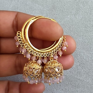 May include: Gold-toned hoop earrings with intricate filigree detailing and dangling pink beads. The earrings feature a bell-shaped charm with clear and pink accents. A stylish accessory for any occasion.