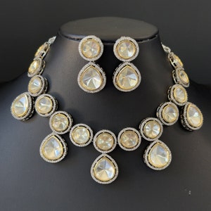 May include: A silver and gold necklace and earrings set with large, clear, faceted stones. The necklace features a teardrop-shaped pendant and round stones.