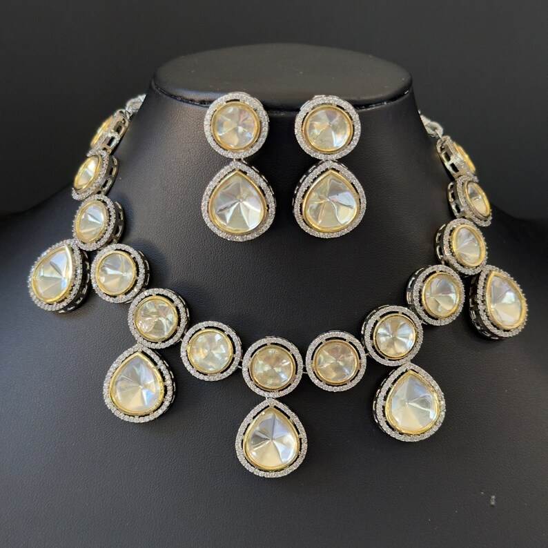 May include: A silver and gold necklace and earrings set with large, clear, faceted stones. The necklace features a teardrop-shaped pendant and round stones.