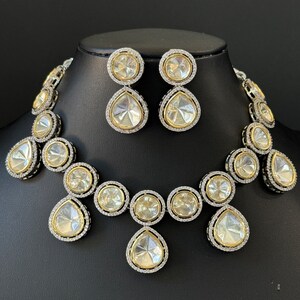 May include: A silver and gold necklace and earrings set with large, clear, teardrop-shaped stones surrounded by smaller, clear stones.