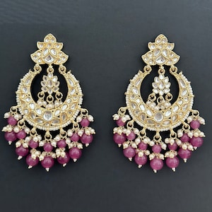 May include: A pair of gold earrings with a crescent moon design, adorned with white stones and pink beads.