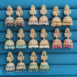 May include: A collection of gold-toned, ornate earrings with various gemstone colors, including pink, green, blue, and white. Each earring features a detailed design with dangling beads, showcasing a traditional jewelry style.