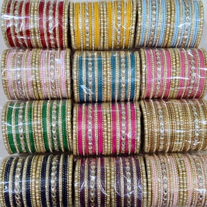 May include: A collection of colorful bangles in various shades, including red, yellow, blue, pink, green, and purple. Each bangle is adorned with gold-colored accents and small, decorative stones, creating a vibrant and ornate appearance. The bangles are arranged in neat rows.