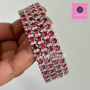 May include: A set of four silver bangles with red and white stones. The bangles are stacked on top of each other and are decorated with a pattern of small, round stones.