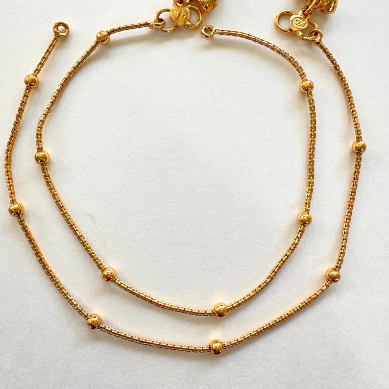 K&ouml;nnte beinhalten: Zwei goldene Fu&szlig;kettchen mit kleinen runden Perlen. Die Fu&szlig;kettchen bestehen aus einer zarten Kette.