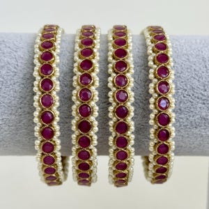 May include: Set of four gold bangles with pink gemstones and white pearl accents.