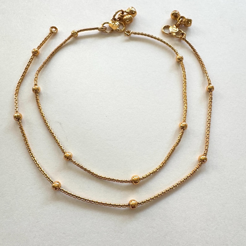K&ouml;nnte beinhalten: Ein Paar goldene Fu&szlig;kettchen mit kleinen runden Perlen. Die Fu&szlig;kettchen bestehen aus einer zarten Kette und haben ein schlichtes Design.