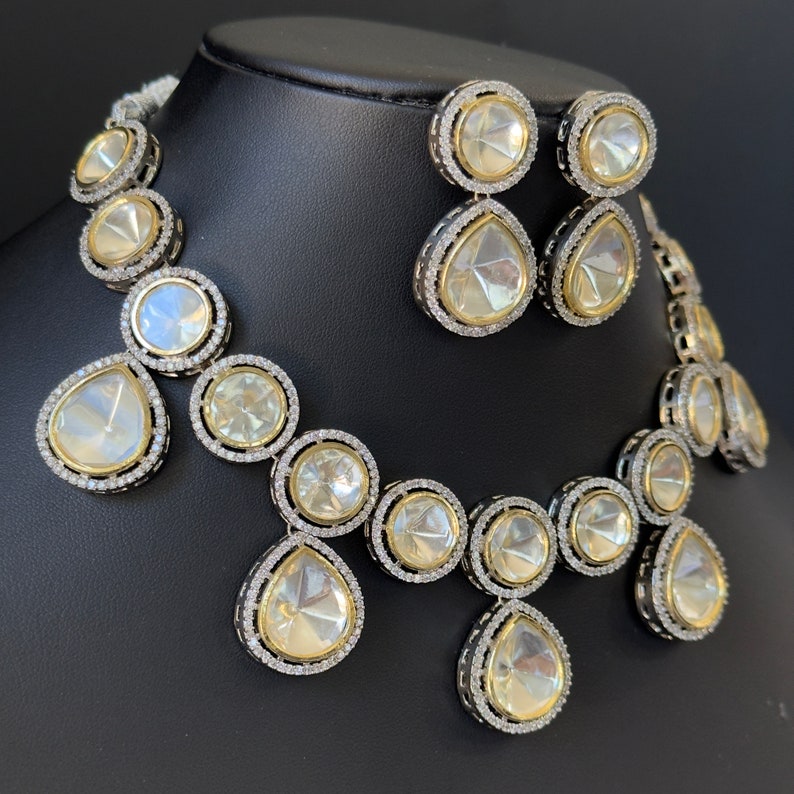 May include: A silver and gold necklace and earrings set with large clear stones. The necklace has a teardrop design with round stones in between. The earrings are teardrop shaped with a round stone at the top.