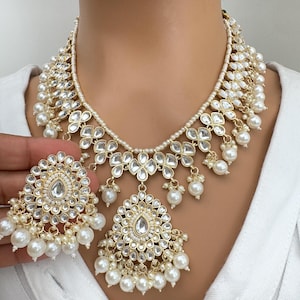 May include: A gold necklace with white pearl accents and a matching pair of earrings. The necklace features a large, ornate pendant with a teardrop-shaped center stone.