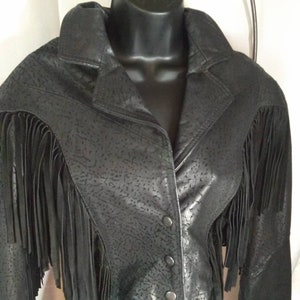 May include: A black leather jacket with fringe detailing on the sleeves and hem. The jacket has a textured surface and a button closure.