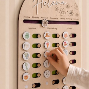 Könnte beinhalten: Ein bogenförmiges hölzernes Tagesplan-Board mit dem Namen Helena in Schreibschrift, Wochentagen und Tageszeiten auf Deutsch. Es enthält einen verschiebbaren Blumen-Marker sowie mehrere runde Holzplättchen mit bunten Aktivitäts-Symbolen.