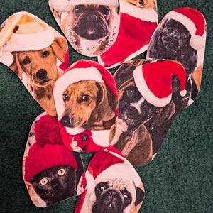 Pode incluir: Uma coleção de oito enfeites de Natal com diferentes raças de cães usando chapéus de Papai Noel. Os enfeites são feitos de feltro e têm um esquema de cores vermelho e branco festivo.