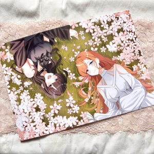 May include: An anime-style print featuring two female characters lying on a grassy field surrounded by white and pink cherry blossoms. One character has brown hair and wears a black outfit, while the other has orange hair and wears a white dress.