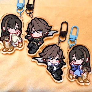 Puede incluir: Varios llaveros acrílicos con personajes de estilo anime y perros. Los llaveros tienen contornos negros y están sujetos a cierres metálicos azules y negros. Los personajes visten varios atuendos.