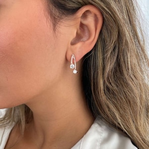 May include: Silver hoop earrings with two small clear cubic zirconia stones. The earrings are curved and have a minimalist design.