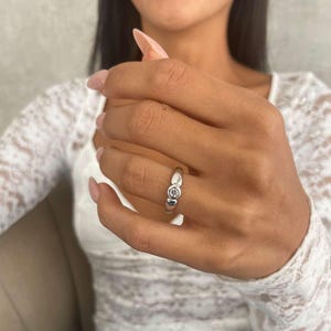 Op de afbeelding: Een zilveren ring met drie heldere, ronde edelstenen. De ring wordt getoond op een hand, met een witte kanten top en een blauwe spijkerbroek op de achtergrond. De edelstenen zijn in een rij geplaatst.