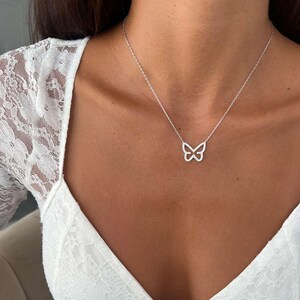 May include: A silver butterfly pendant necklace. The butterfly design is encrusted with small, sparkling stones. The necklace is worn on a person with a white lace top.