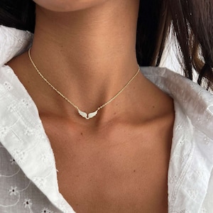 May include: A gold chain necklace with a small, delicate pair of angel wings pendant. The wings are encrusted with tiny, sparkling stones.