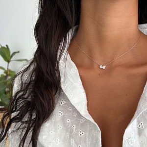 May include: A delicate gold chain necklace with two small pear-shaped clear stones. The necklace is worn by a person with long dark hair and a white shirt.
