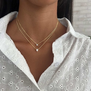 Könnte beinhalten: Eine goldene Kettenkette mit zwei kleinen Diamantanhängern. Die Kette ist geschichtet und verfügt über einen runden Diamantanhänger und einen birnenförmigen Diamantanhänger.