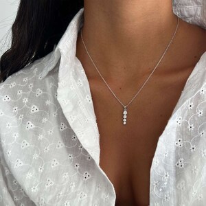 Puede incluir: Un collar de cadena de plata con un colgante que presenta una fila de cinco pequeñas piedras preciosas transparentes.