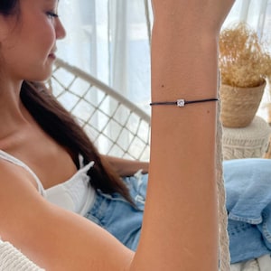 May include: A simple black string bracelet with a single clear cubic zirconia stone.