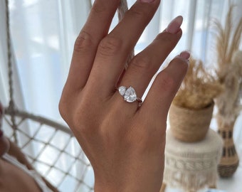 Op de afbeelding: Een zilveren ring met twee heldere, peervormige stenen. De ring zit aan een vinger.