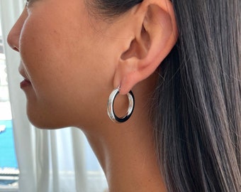 May include: Silver hoop earrings with a black enamel inlay. The earrings are worn by a person with long black hair.