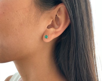 Puede incluir: Un par de pequeños pendientes de botón redondos de color verde esmeralda. Los pendientes están engastados en un engaste de metal plateado.