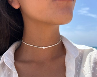 May include: A delicate silver choker necklace with a single small sparkling diamond in the center.