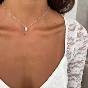 May include: A delicate rose gold necklace featuring a marquise-cut diamond pendant. The pendant is suspended from a fine chain, creating a minimalist and elegant look. The necklace is shown against a backdrop of a white lace top.