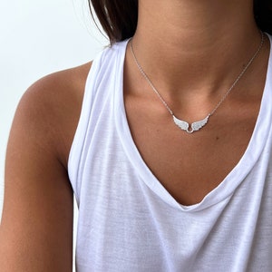 Puede incluir: Un collar de plata con una cadena delicada y un peque&ntilde;o colgante de ala incrustado con piedras de circonita c&uacute;bica transparentes.