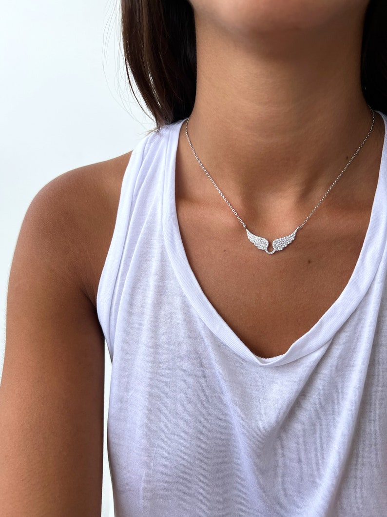 Puede incluir: Un collar de plata con una cadena delicada y un peque&ntilde;o colgante de ala incrustado con piedras de circonita c&uacute;bica transparentes.
