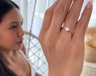 Può includere: Un delicato anello in oro rosa con una piccola pietra preziosa a forma di cuore trasparente.
