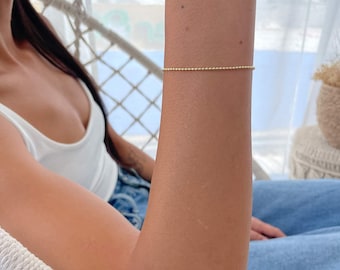 Puede incluir: Un brazalete de cadena dorada con pequeñas cuentas redondas.