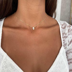 May include: A delicate gold necklace with a small, teardrop-shaped pendant. The pendant is a clear, sparkling stone. The necklace is worn on a person wearing a white lace top.