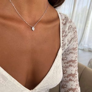 May include: A delicate silver necklace featuring a marquise-cut pendant. The pendant is suspended from a fine chain. The necklace is shown against a white lace top.