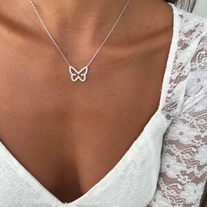 May include: A silver butterfly pendant necklace. The pendant is a delicate openwork design in the shape of a butterfly. The necklace is worn on a person with a white lace top.