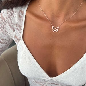 May include: A delicate rose gold butterfly pendant necklace. The butterfly design is encrusted with small, sparkling stones. The necklace is worn on a person wearing a white lace top.