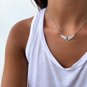 Puede incluir: Un collar de plata con una cadena delicada y un colgante de ala de diamante brillante.