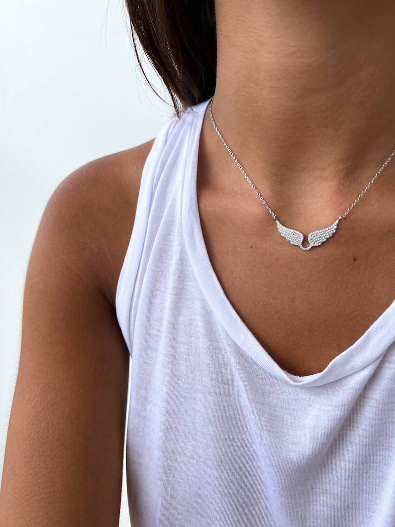 Puede incluir: Un collar de plata con una cadena delicada y un colgante de ala de diamante brillante.