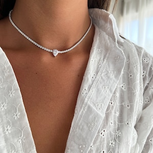 Peut inclure: Un collier ras de cou argent&eacute; avec un pendentif en diamant de forme poire. Le collier est compos&eacute; de petites pierres claires.