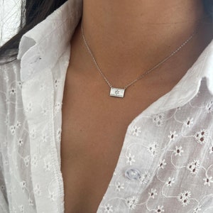May include: A silver chain necklace with a small rectangular pendant featuring a Star of David design. The pendant is set with small clear stones.
