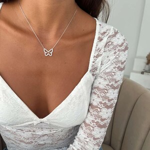 May include: A silver butterfly pendant necklace. The necklace features a delicate butterfly design suspended from a fine chain. The butterfly pendant is openwork, showcasing the intricate details of the design. The necklace is worn with a white lace top.